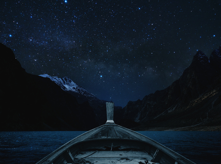 Travelling on lake at night by boat, sky full of star and milky way with mountains valleyの写真素材