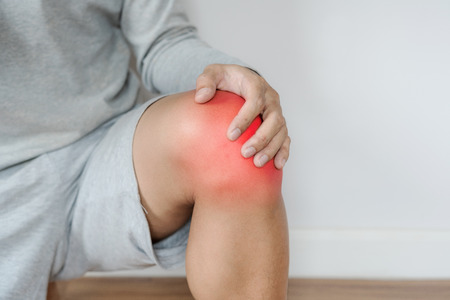 a man touching knee with red highlights concept of knee and joint painの写真素材