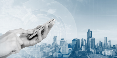Mobile smart phone technology, hand touching mobile phone and city backgroundの写真素材