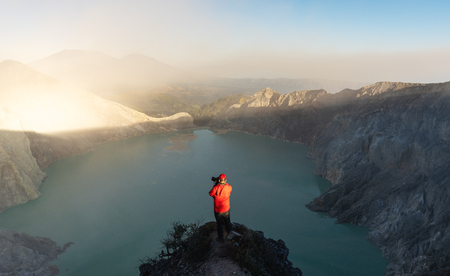 Traveller taking photograph on sightseeing point at kawah Ijen volcanic lake in the morning, famous tourist attraction and travel destination in Indonesiaの写真素材
