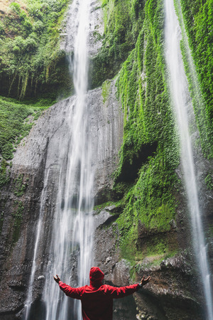 Traveller in red jacket raised hand, at Madakaripura waterfall in Indonesia. Travel lifestyle and successの写真素材