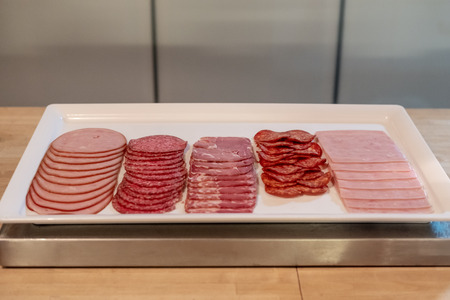 Slices various type of meat, sausage, salami and hams on white trayの写真素材