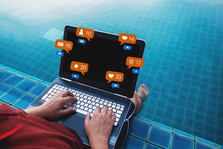 a man using computer laptop at poolside in summer holiday, with social media, social network notification iconsの写真素材