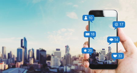 Hand holding mobile smart phone, with notification icons and city backgroundの写真素材