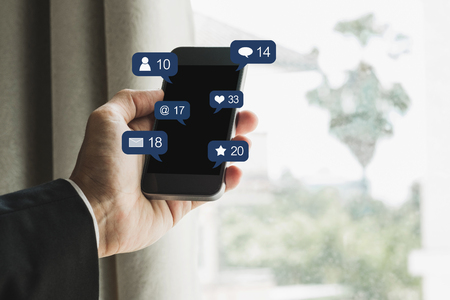 Hand holding mobile smart phone, with social media and social network notification iconの写真素材