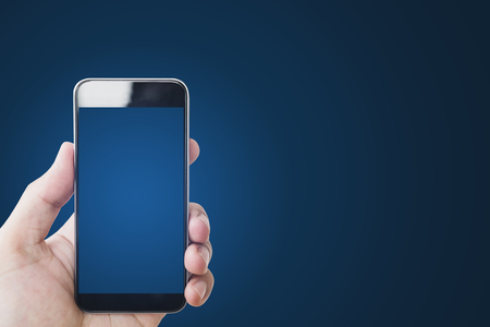 Hand holding mobile smart phone, blank blue screen, on gradient blue backgroundの写真素材