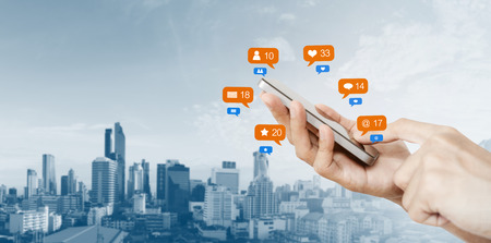 Hand holding mobile smart phone, with notification icons and city backgroundの写真素材