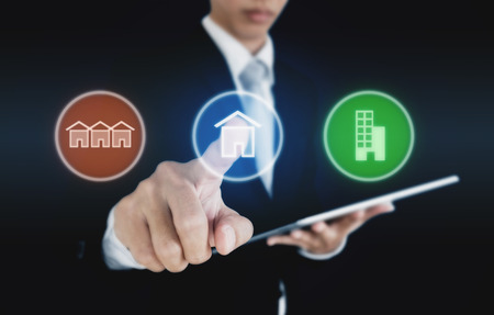 Businessman pressing real estate icons on screen. Business investment in real estate, town house, single home and condominiumの写真素材