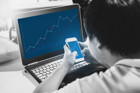 Online business and investment. a man working on computer laptop and mobile smart phone, raising graph on screenの写真素材