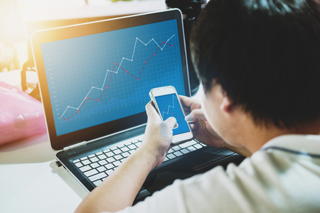 Online business and investment. a man working on computer laptop and mobile smart phone, raising graph on screenの写真素材