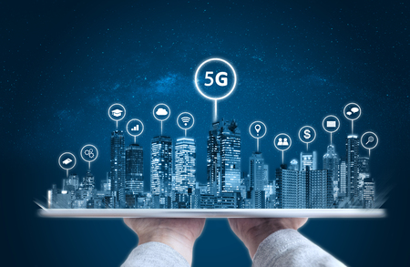 Hand holding digital tablet with modern buildings hologram and technology icons. Smart city, 5g, internet and networking technology conceptの写真素材