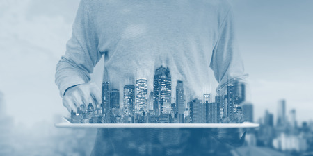 a man using digital tablet with modern buildings hologram. Real estate business and investment, building technologyの写真素材