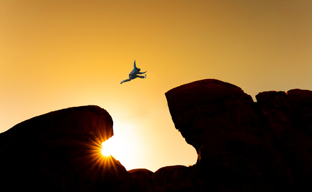 Challenge, risk and freedom concept. Silhouette a man jumping over precipice crossing cliffの写真素材