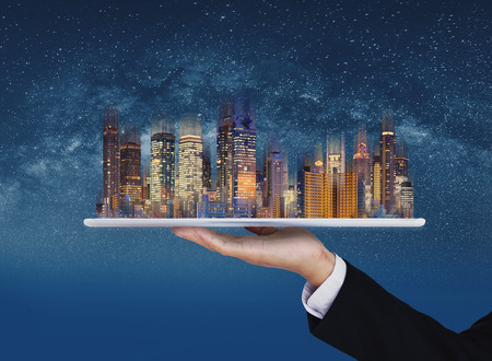 Real estate business, smart city, and building technology. Businessman hand holding digital tablet with buildings hologram and stars backgroundの写真素材