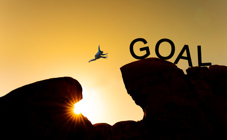 Silhouette a man jumping over precipice to goal. Achieve goal, business goals, challenge and success conceptの写真素材