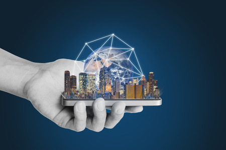 Smart technology, smart city and network technology. Hand holding mobile smart phone with buildings global network hologram.の写真素材