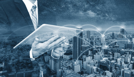 Business network, blockchain technology and internet connection. Double exposure businessman using digital tablet, and cityscapeの写真素材