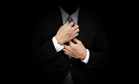Businessman in black suit tying necktie, on black backgroundの写真素材