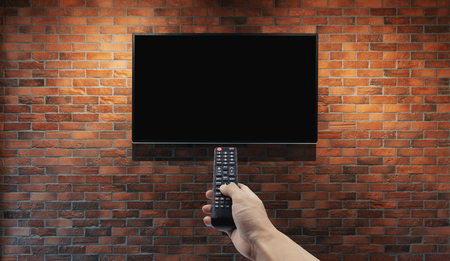 Television on brick wall with hand using remote controlの写真素材