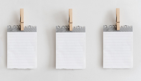 Paper note and wooden paper clip hanging on white wall