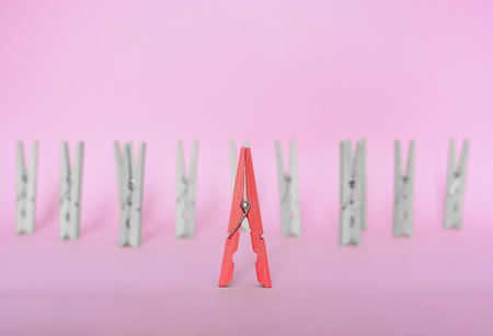 Unique, individuality, outstanding,leadership and think different concept. Red wooden clip stand out of colorless clips on pink backgroundsの写真素材