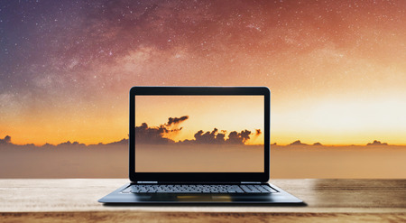 Computer laptop on wooden desk and sunrise sky with stars backgroundの写真素材