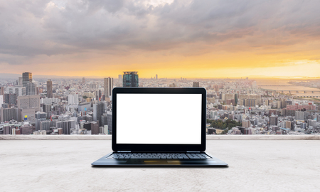 Computer laptop blank white screen on white concrete desk and Osaka city sunset view in Japan. Laptop Computer Backgroundの写真素材