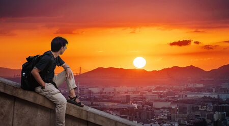 a man with backpack looking at Osaka city view in sunset with the sunの写真素材