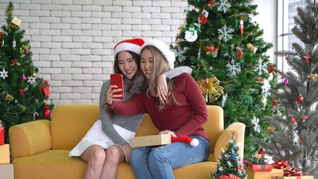 Asian women smiling and showing gift, taking a selfie by mobile smartphone in Christmas holidayの写真素材