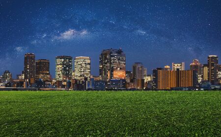 Modern buildings with green grass in the city at night with starry sky. City Backgroundsの写真素材