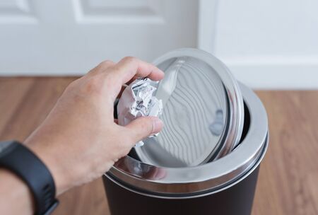 Hand putting crumpled bill paper in trash canの写真素材