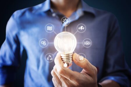 Businessman holding bright light bulb with energy resources icons