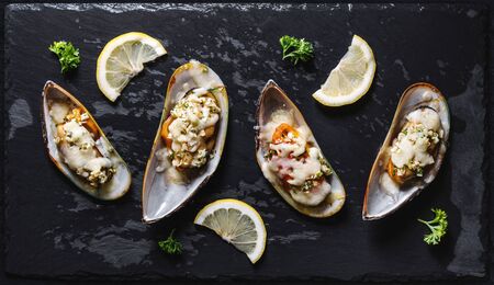 New Zealand Mussels baked with butter, garlic, parsley and cheese, on black stone plateの写真素材
