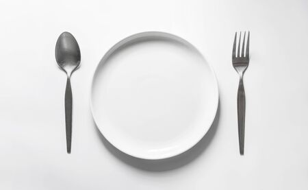 Ceramic round dish with silver fork and spoon, on white tableの写真素材