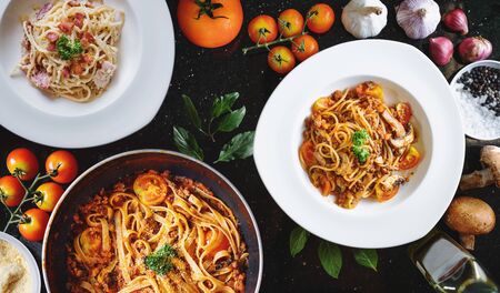 Italian food, Pasta Bolognese, tomatoes sauce, and Carbonara with fresh ingredients, on black tableの写真素材