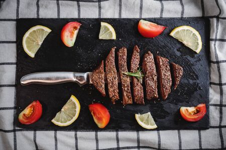 Grilled beef steak, Tenderloin on black stone plate with Rosemary, tomatoes and lemonの写真素材