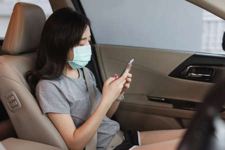 Asian woman wearing protective face mask and using mobile smartphone in modern car. New normal, corona virus and air pollution conceptの写真素材