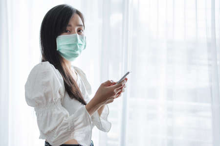 Asian woman wearing protective face mask, and using mobile smartphoneの写真素材