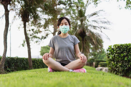 Young Asian woman wearing face mask and meditating in parkの写真素材