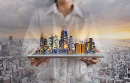 Double exposure businesswoman holding digital tablet with building hologram and city sunrise backgroundの写真素材