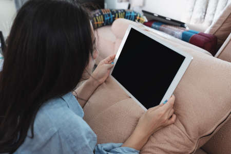 Young woman using digital tablet, in living room with isolated black screen