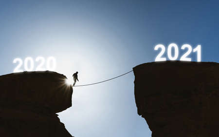 2021 new year concept, silhouette a man walking on rope from 2020 to 2021