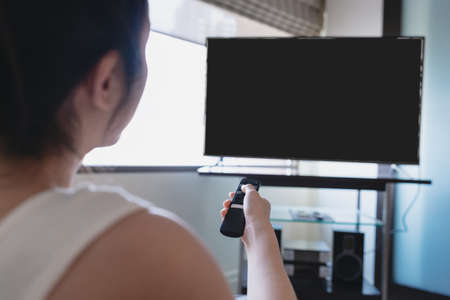 Woman holding tv remote control opening digital smart television in living roomの写真素材