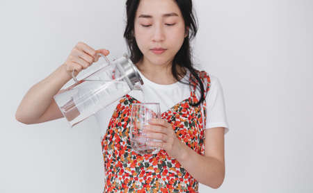 Healthy beautiful young Asian woman, pouting fresh water on drinking glass, on white background