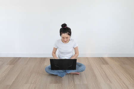 Young Asian woman using computer laptop, in empty living roomの写真素材