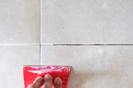 Floor tile fixing and renovation, Hand using trowel repairing old tile grout in bathroomの写真素材