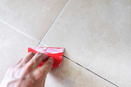Floor tile fixing and renovation, Hand using trowel repairing old tile grout in bathroomの写真素材