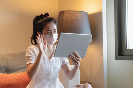 Asian woman wearing medical face mask, and using digital tablet for video conference, online meetingの写真素材