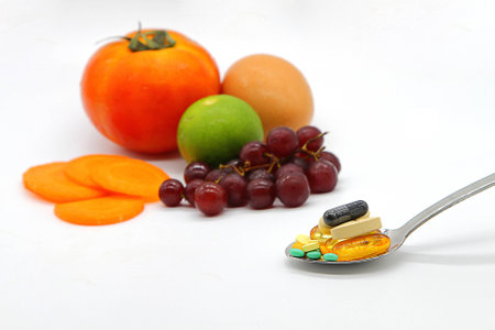 Assorted vitamins and nutritional supplements in serving spoon on blur colorful fruits backgroundの写真素材