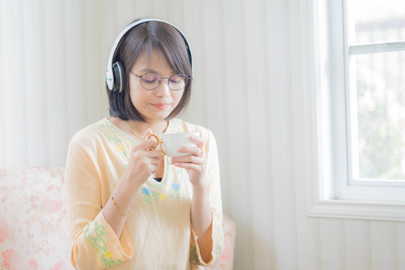 Beautiful young woman with headphones and smartphone relaxing on sofa .she is listening to music using a smartphone in the coffe shope.の写真素材